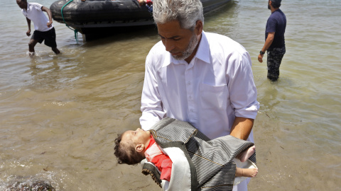 Guardacostas libios sostienen los cadáveres de tres bebés fallecidos en el naufragio frente a las costas libias. Hay cien desaparecidos y 16 supervivientes.- AFP/ MAHMUD TURKIA