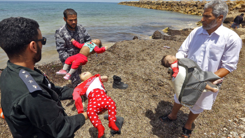 Guardacostas libios sostienes los cadáveres de tres bebés fallecidos en el naufragio frente a las costas libias. Hay cien desaparecidos y 16 supervivientes.- AFP/ MAHMUD TURKIA