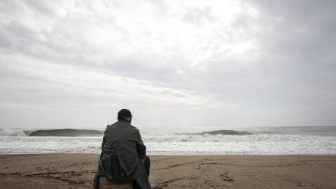 Un hombre mira al  mar en una playa mientras está nublado.