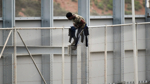 Un migrante encaramado a la valla fronteriza que separa Ceuta de Marruecos, este martes 13 de abril,