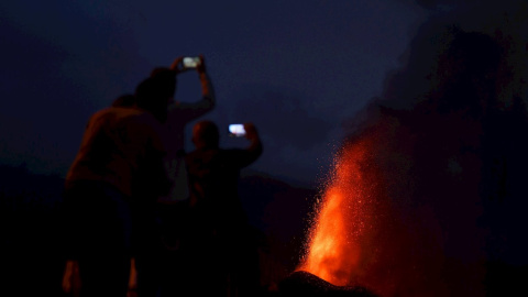 Cuatro personas contemplan desde una montaña al caer la noche la lava que sale del volcán de La Palma este lunes 20 de septiembre de 2021.