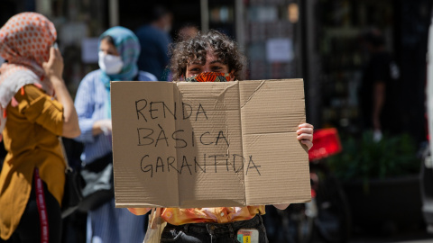 Una dona, acompanyada per membres de la Xarxa veïnal de Suport Mutu Ciutat Vella, agafa una pancarta en la qual es pot llegir "Renda bàsica garantida". 22 de maig del 2020.