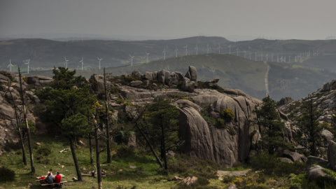 Una familia come en el área recreativa del Monte Pindo, con los molinos al fondo en las montañas.