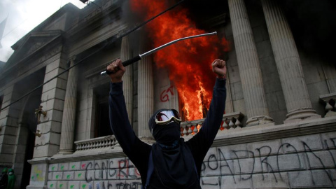 Un hombre protesta en frente del Congreso de Guatemala en llamas ocasionado por manifestantes que protestan contra del Gobierno del presidente, Alejandro Giammattei hoy en Ciudad de Guatemala (Guatemala). Cientos de manifestantes tomaron este sábado el C