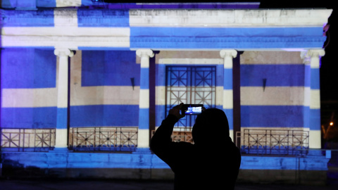 Un hombre toma fotografías frente al antiguo ayuntamiento de Nicosia, iluminado con la bandera griega que marca el 200 aniversario de la Guerra de Independencia de Grecia, en Nicosia, Chipre, el 25 de marzo de 2021.