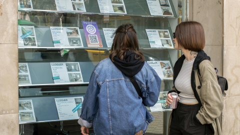 Dos personas observan la oferta de pisos en alquiler de una oficina inmobiliaria de Barcelona, a 12 de marzo de 2024.