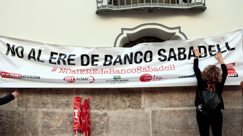 Una persona cuelga una pancarta en la fachada del banco Sabadell en Valencia