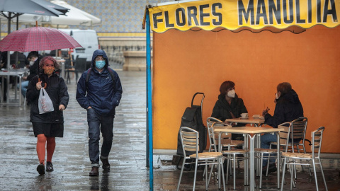 Dos personas en la terraza de un bar protegidas de la lluvia por un toldo de un puesto de flores.