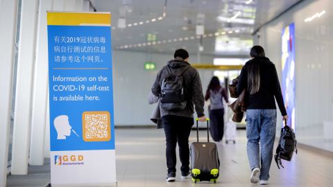 Viajeros de China pasan frente a una pancarta con información y reciben un test de covid-19 a su llegada a Schiphol, Países Bajos, el 04 de enero de 2023.