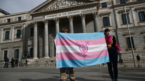 Dos personas sostienen una bandera trans durante una concentración convocada frente al Congreso de los Diputados en Madrid.