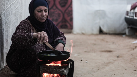 Mujer palestina desplazada cocina fuera de su tienda de campaña.