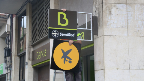 Un operari canviant el logotip de Bankia pel de CaixaBank a l'oficina situada al número 116 de la Rambla del Poblenou de Barcelona. Imatge de 6 d'abril de 2021.