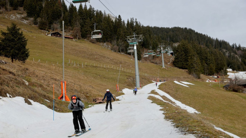 Esquiadores pasan sobre una pequeña capa de nieve en medio de temperaturas invernales más cálidas de lo habitual en los Alpes en Leysin, Suiza, a 4 de enero de 2023