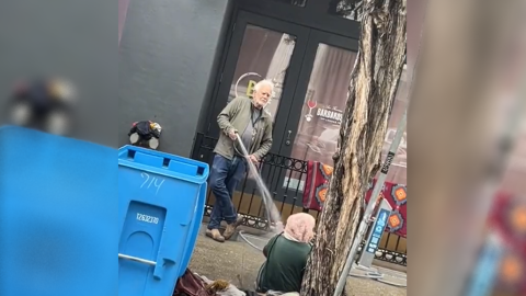 Un hombre rociando con agua a una mujer sin hogar en San Francisco. — @briochesf / TIK TOK