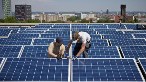 Dos operarios instalan paneles solares en el tejado de un edificios.