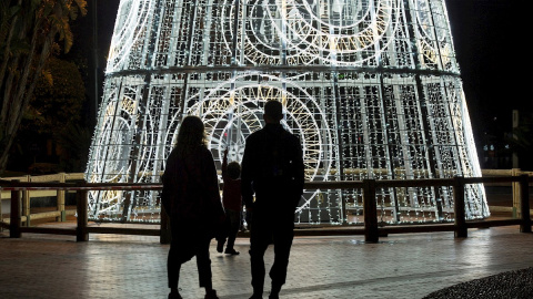 Una pareja y su hijo observan un árbol de navidad iluminado en la Plaza de la Marina, en Málaga.