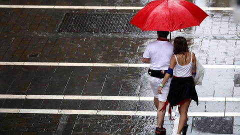 Dos personas se protegen de la lluvia en una de las céntricas calles de Pamplona durante la fiesta de San Fermín. Navarra está en alerta amarilla este lunes por lluvias y tormentas, según Aemet. EFE/ Javier Lizón