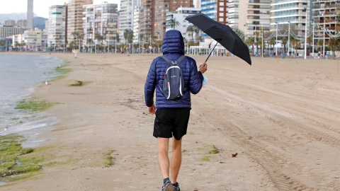 Una persona se protege de la lluvia con un paraguas mientras pasea por la playa de Levante de Benidorm