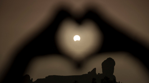 Una mujer hace el gesto del corazón con las manos enmarcando el eclipse de Sol, en el Roque Nublo, en Gran Canaria. REUTERS/Borja Suarez