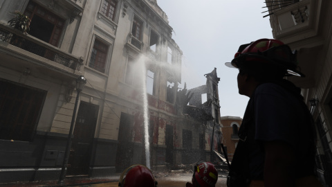 Bomberos trabajan en los alrededores de una casona que se incendió ayer durante la jornada de protestas en Lima.