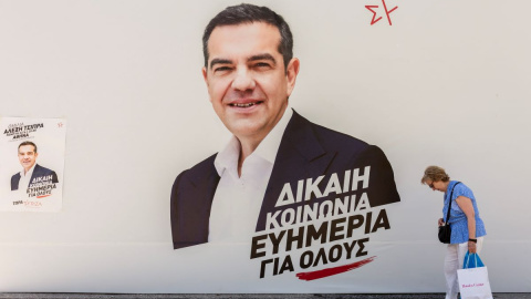 Una mujer pasa por delante de un puesto de campaña de Syriza con una foto del líder del partido Alexis Tsipras en el centro, a 25 de junio de 2023, en Atenas.