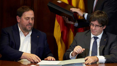 El presidente de la Generalitat, Carles Puigdemont (derecha), acompañado por el vicepresidente Oriol Junqueras, firma la convocatoria de referéndum. | ALEJANDRO GARCÍA (EFE)