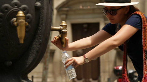 07/2023 - Una mujer llenando una botella en una fuente de agua de Barcelona.