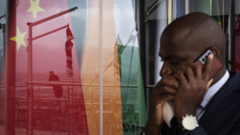 Un hombre habla por su teléfono móvil mientras pasa por una ventana en la que se reflejan las banderas de los BRICS, a 2 de junio de 2023 en Cape Town