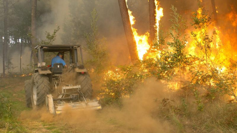 Un hombre subido en un tractor se sitúa frente al fuego del incendio de Zamanes, Vigo. EFE/Salvador Sas