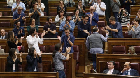 Joan Mena, de espaldas, sube a su escaño entre los aplausos de Podemos. / EFE