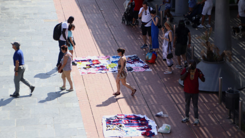 Venedors ambulants interactuen amb compradors en una plaça del front marítim