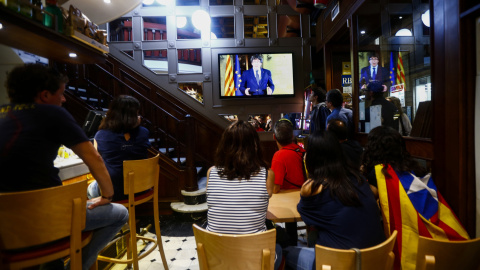 Un grupo de ciudadanos siguen desde una pantalla de televisión la declaración institucional del presidente de la Generalitat, Carles Puigdemont, tras la decisión del Gobierno de aplicar el artículo 155 en Cataluña. EFE/Quique García