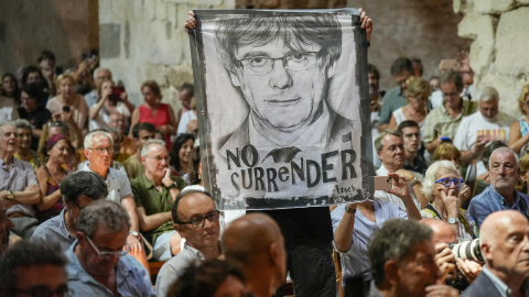 Un asistente sostiene una pancarta con la cara de Carles Puigdemont y la frase "No Surrender" este lunes en la abadía de Sant Miquel de Cuixà, en Codalet (Francia).