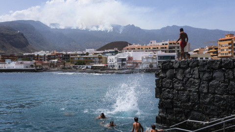 Varias personas disfrutan este lunes de un día de playa en el Puertito de Güímar, desde donde se puede ver el incendio que afecta a la isla de Tenerife desde hace seis días.