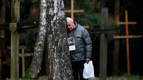 Un hombre reposa su cabeza contra un árbol en Kuropaty, donde se rinde homenaje a las víctimas del estalinismo./REUTERS