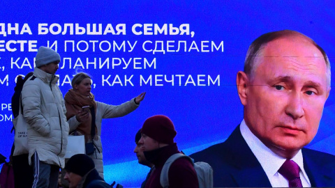 Un grupo de transeúntes pasan cerca de una pantalla digital que muestra una imagen Vladimir Putin, en San Petersburgo, a 14 de marzo de 2024.