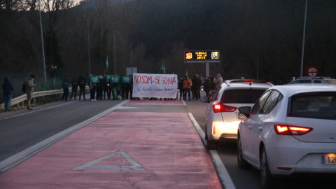 Els manifestants al fons protestant mentre els conductors esperen aturats pel tall de la carretera a Ripoll.