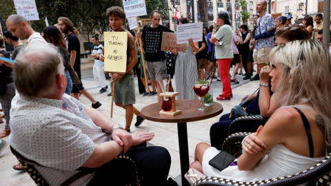 Unos turistas sentados en la terraza de un bar ven marchar una manifestación contra el turismo masivo, en Alicante. REUTERS/Eva Manez