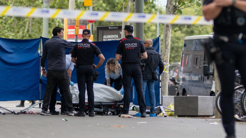 Agentes de los Mossos d'Esquadra y trabajadores de la funeraria levantan el cadáver del joven fallecido, en el paseo Joan de Borbó, en Catalunya.