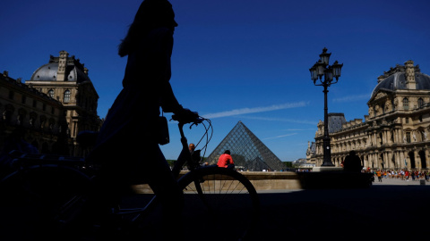 11/05/2022-Una mujer camina con su bicicleta cerca de la Pirámide de cristal del museo del Louvre París, Francia, el 11 de mayo