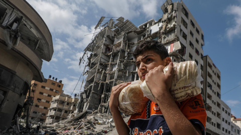 16/10/23 Un joven palestino porta dos bolsas de pan este lunes 16 de octubre frente a un edificio bombardeado en el barrio de Al Remal, en la ciudad de Gaza.