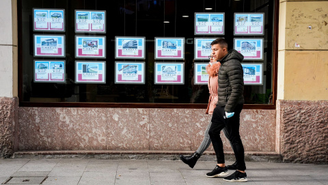 Una pareja joven pasa por delante del escaparate de la oficina de una inmobiliaria, en Guernica (Vizcaya). REUTERS/Vincent West