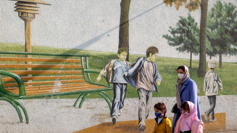 Una mujer pasea junto a sus hijos frente a un mural infantil en Teherán.