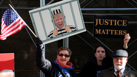 Manifestantes sostienen una imagen que muestra a Trump tras las rejas y un cartel que dice "La justicia importa" durante una protesta contra el ex presidente estadounidense Trump frente a un tribunal.