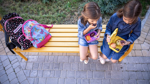 Niñas de la escuela sentadas en un banco en el patio de la escuela y comiendo de las loncheras