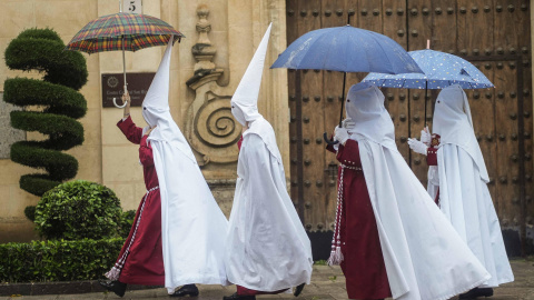 Unos nazarenos de la Hermandad de La Sentencia se protegen de la lluvia con paraguas en Córdoba este lunes 25 de marzo de 2024.