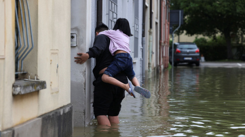 Un hombre y una niña abandonan su vivienda tras las fuertes inundaciones en la región de Emilia Romaña, en el noreste de Italia.