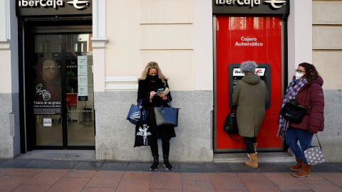 Una mujer utiliza el cajero automático de una oficina de Ibercaja en Madrid, mientras otras esperan. REUTERS/Juan Medina