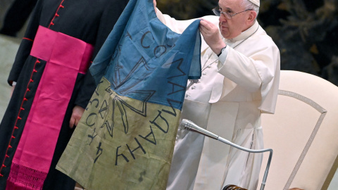 12/04/2022 - El papa Francisco muestra una bandera de Ucrania que fue enviada desde la localidad de Bucha durante la audiencia semanal en el Salón de Pablo VI en el Vaticano.