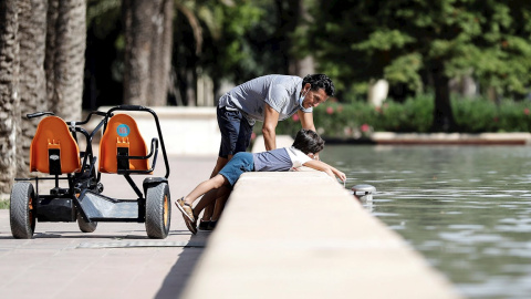 Un padre y su hijo se refrescan en una fuente de Valencia.